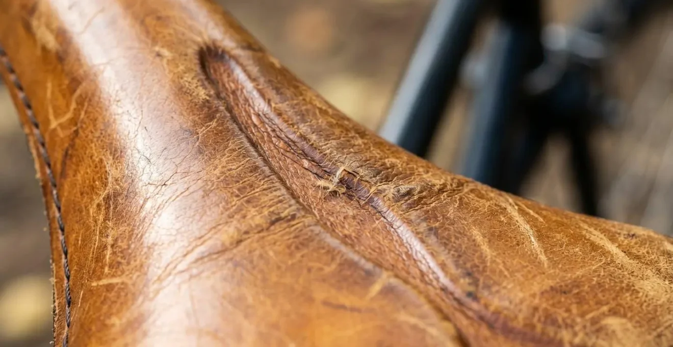 Gros plan macro sur la texture d'une selle en cuir patiné montrant les plis naturels formés par le rodage et l'adaptation à la morphologie du cycliste